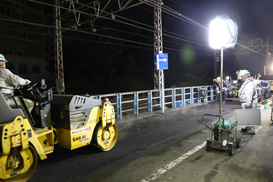 A battery light tower illuminates road maintenance work.